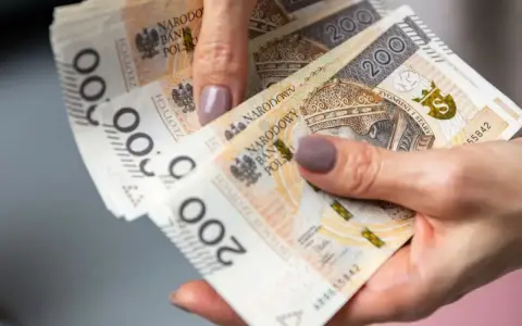 Dłonie trzymające polskie banknoty 200 zł. Czy można pobierać 500 plus i Kindergeld?