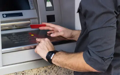 Mężczyzna wkłada kartę do bankomatu, przygotowując się, jak wypłacić pieniądze z bankomatu za granicą.
