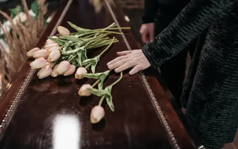 Dłoń na trumnie z tulipanami. W Niemczech zasiłek pogrzebowy może pomóc w pokryciu kosztów.