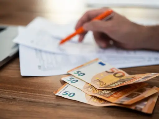 Rozłąkowe w Niemczech: stos 50 euro na biurku, ręka z długopisem nad dokumentami.