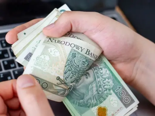 Ręce trzymające stos banknotów 100 zł na tle klawiatury laptopa. Czy w Żabce można wpłacić pieniądze?