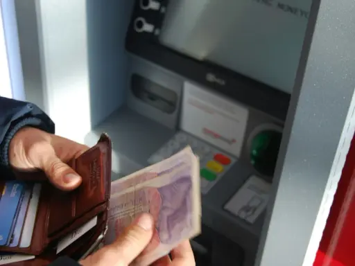 Ręce trzymają portfel i banknoty przy bankomacie. Czy da się wyplacic pieniadze bez karty? Tak, jeśli masz kod PIN.