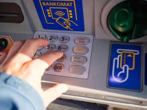 Dłoń wpisuje PIN na bankomacie. Co zrobić, gdy bankomat wciągnął kartę i jak załatwić zwrot?
