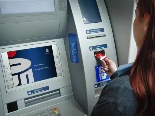 Kobieta wkłada kartę do bankomatu Banku Millennium. Ekran wyświetla powitanie.