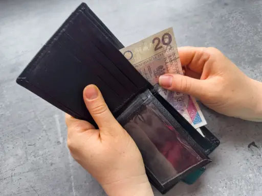 Dłonie wkładają banknot 20 zł do portfela. Czekasz na zasiłek dla bezrobotnych?