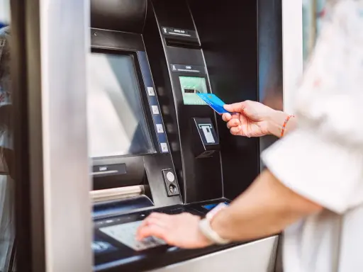 Kobieta wkłada kartę do bankomatu PKO, aby dokonać wypłaty gotówki.