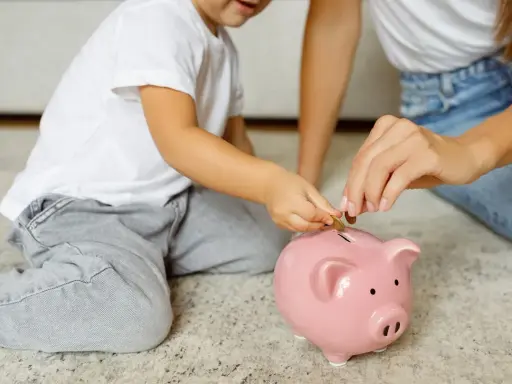 Dziecko i mama wrzucają monety do różowej świnki-skarbonki. Uczą się oszczędzać, by wiedzieć, kto wypłaca rodzinne.