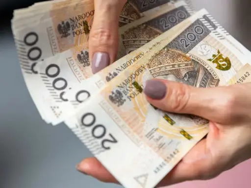 Dłonie trzymające polskie banknoty 200 zł. Czy można pobierać 500 plus i Kindergeld?