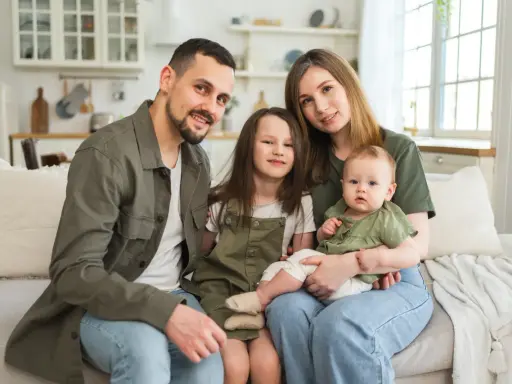 Szczęśliwa rodzina na kanapie. Rodzice z dwójką dzieci, starszą córką i niemowlęciem. Myślą o przyszłości i wsparciu, jak kindergeld po 18 roku życia.