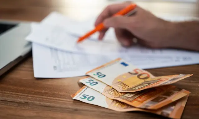Rozłąkowe w Niemczech: stos 50 euro na biurku, ręka z długopisem nad dokumentami.