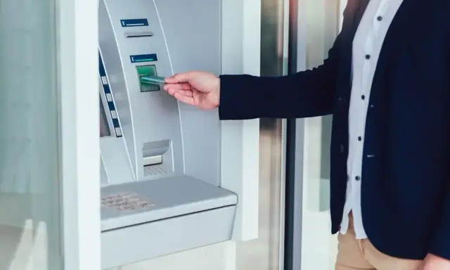 Mężczyzna wkłada kartę do wpłatomatu, który przyjmuje różne banknoty.