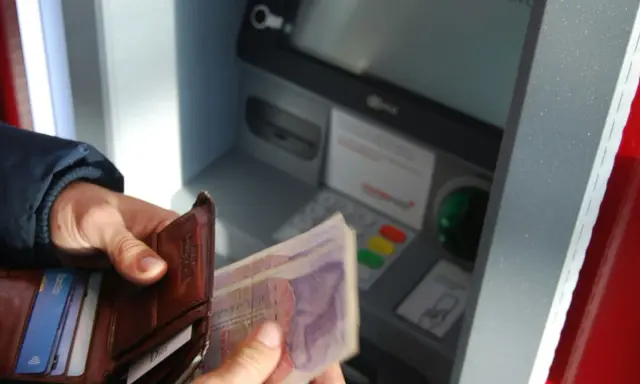 Ręce trzymają portfel i banknoty przy bankomacie. Czy da się wyplacic pieniadze bez karty? Tak, jeśli masz kod PIN.