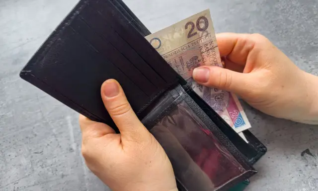 Dłonie wkładają banknot 20 zł do portfela. Czekasz na zasiłek dla bezrobotnych?