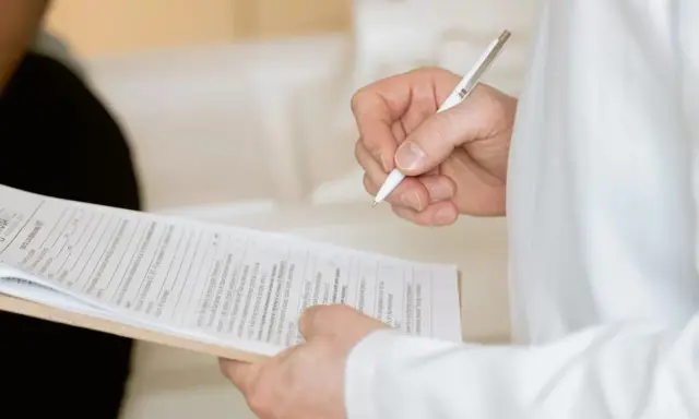 Ręka trzymająca długopis nad dokumentami. Widać fragmenty formularzy, które mogą być związane z Familienkasse druki po polsku.