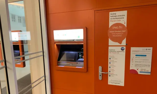 Bankomat Planet Cash z informacją o braku prowizji dla klientów ING. W pobliżu znajduje się też plakat o koronawirusie.