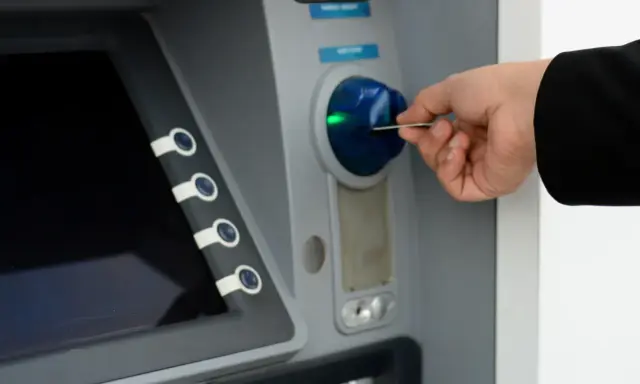 Dłoń wkłada kartę do bankomatu, próbując uzyskać dostęp do środków, ale konto bankowe jest zablokowane.