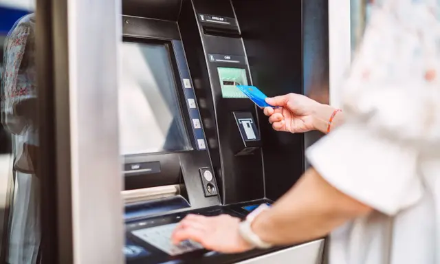 Kobieta wkłada kartę do bankomatu PKO, aby dokonać wypłaty gotówki.