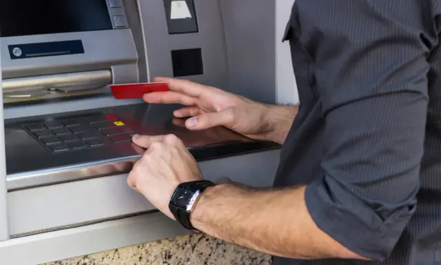 Mężczyzna wkłada kartę do bankomatu, przygotowując się, jak wypłacić pieniądze z bankomatu za granicą.