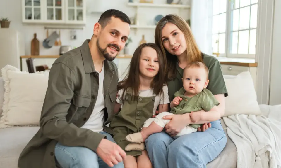 Szczęśliwa rodzina na kanapie. Rodzice z dwójką dzieci, starszą córką i niemowlęciem. Myślą o przyszłości i wsparciu, jak kindergeld po 18 roku życia.