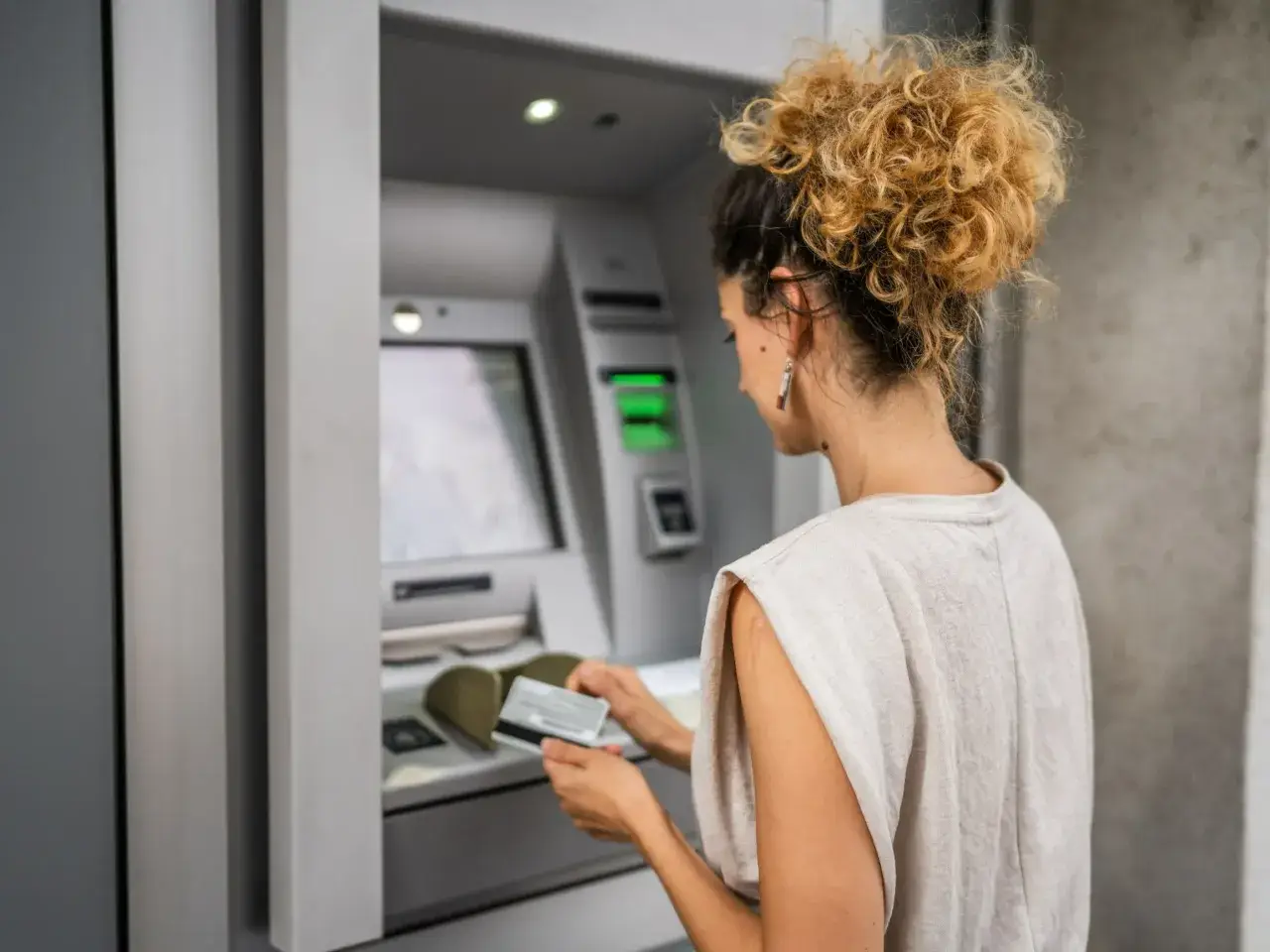 Kobieta z burzą blond loków wkłada kartę do wpłatomatu Santander.