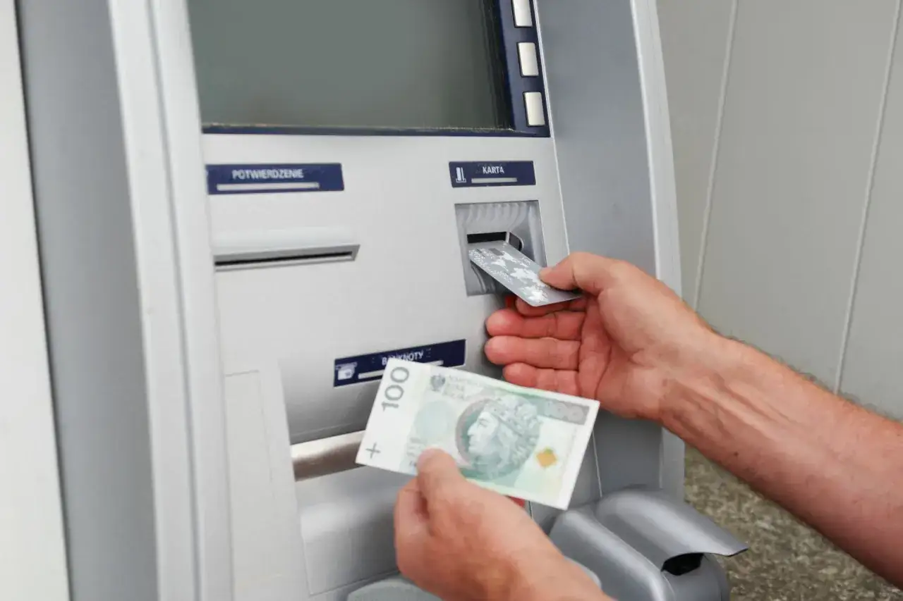 Ręka wkłada kartę do bankomatu, a w drugiej trzyma 100 zł. Zapomniałem, że zostawiłem pieniądze w bankomacie.