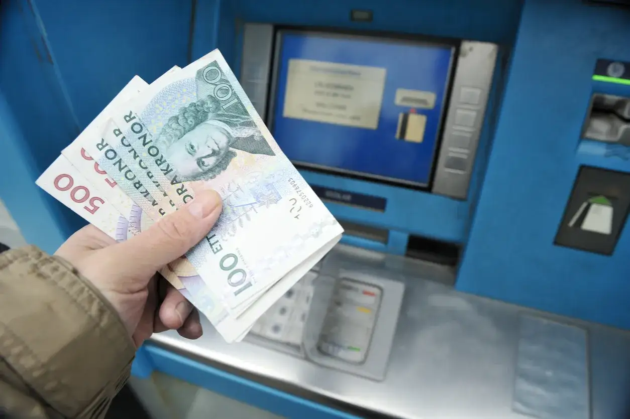 Dłoń trzyma szwedzkie korony przy bankomacie. Czy w Szwecji można płacić euro? Nie, tam obowiązuje korona szwedzka.
