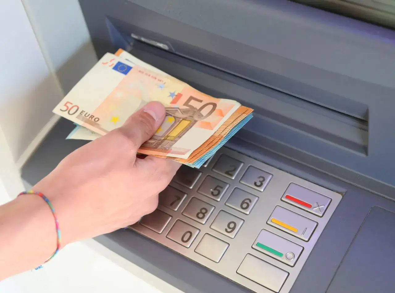Ręka z banknotami 50 euro wyciąga pieniądze z bankomatu. Tak, z bankomatu można wypłacić euro.