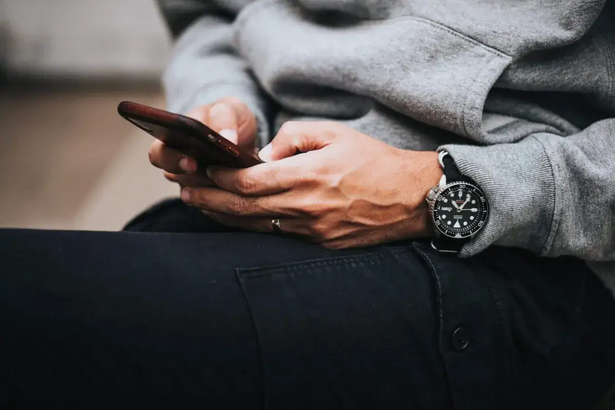 Mężczyzna w szarej bluzie i czarnych spodniach trzyma telefon, gotowy do szybkiej revolut płatność telefonem nfc.