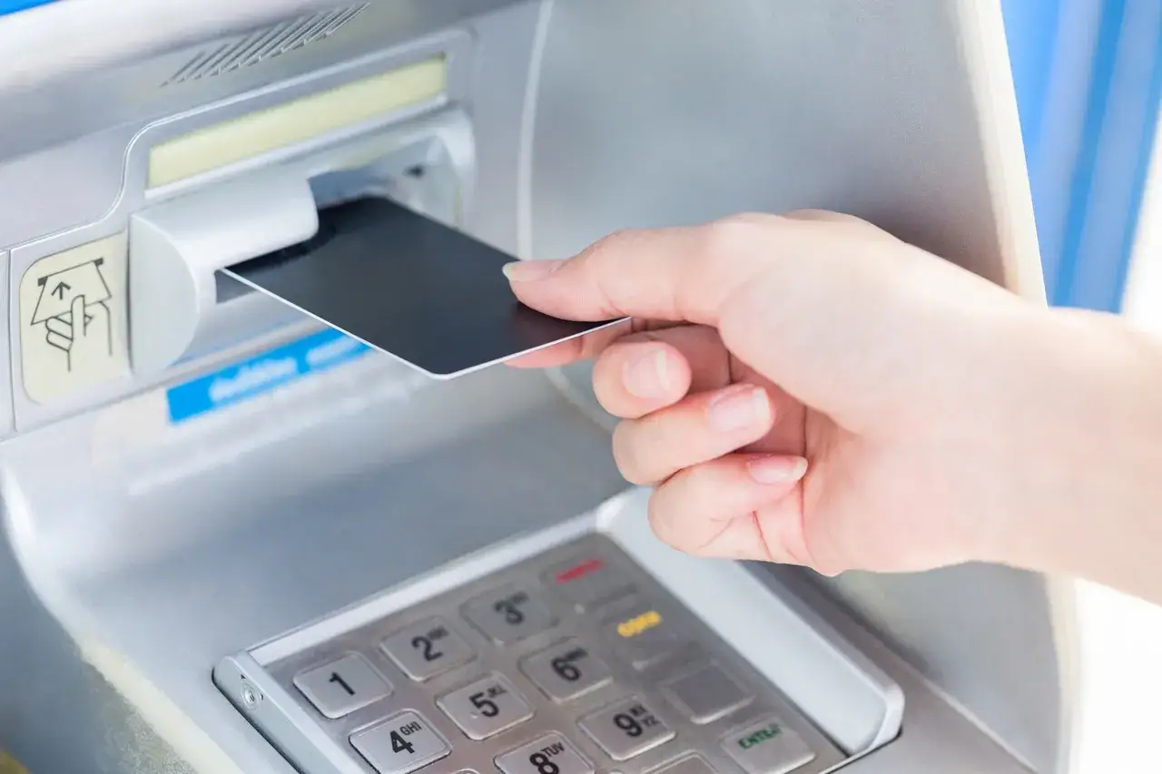 Dłoń wkłada kartę do bankomatu. Wkr&oacute;tce dowiesz się, jak zmienić PIN do karty, aby zwiększyć bezpieczeństwo.