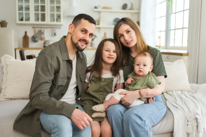 Szczęśliwa rodzina na kanapie. Rodzice z dwójką dzieci, starszą córką i niemowlęciem. Myślą o przyszłości i wsparciu, jak kindergeld po 18 roku życia.